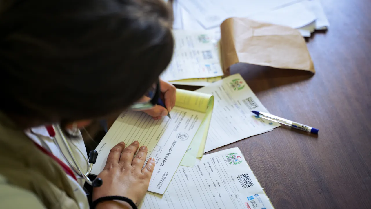 Healthcare worker completing medical paperwork and documentation on a desk.