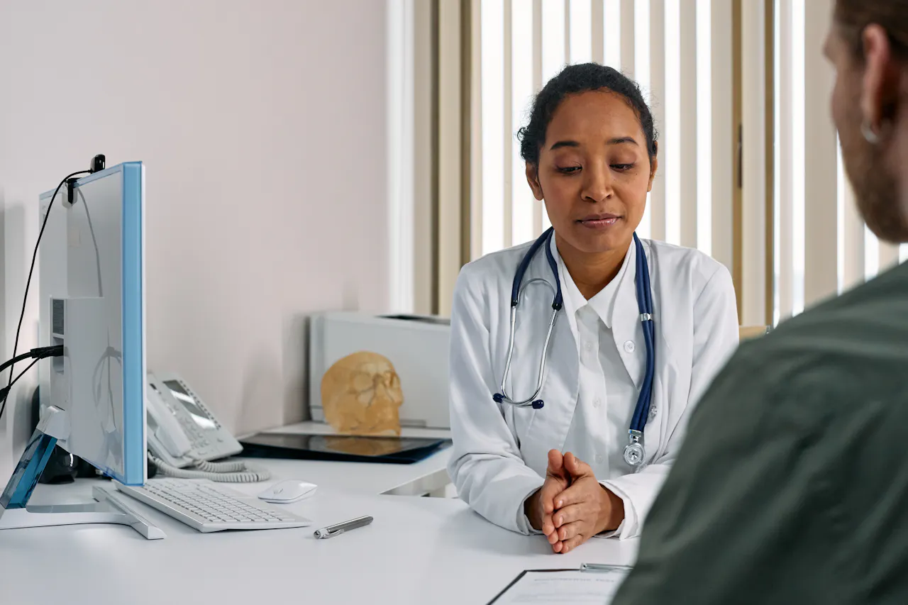Doctor in consultation with a patient across a desk in a clinic.